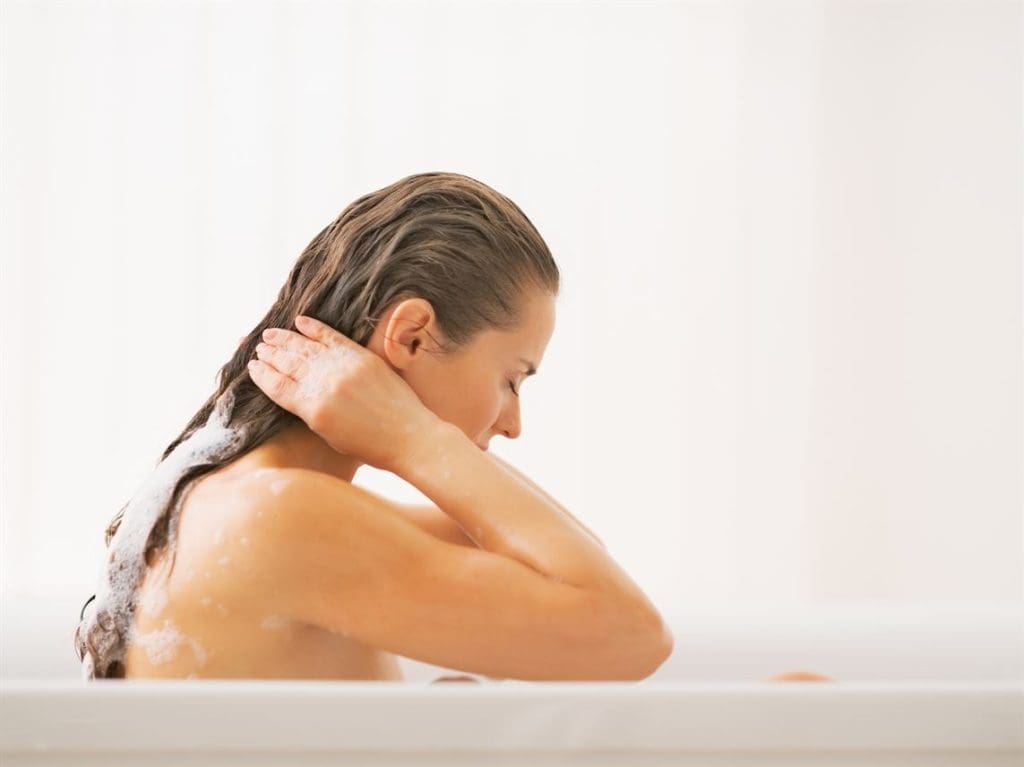 Young woman washing hair in bathtub